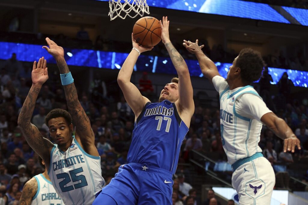 Dallas Mavericks guard Luka Doncic (77) shoots against Charlotte Hornets forward P.J. Washington (25) and guard Theo Maledon, right, in the second half of an NBA basketball game Sunday, Nov. 5, 2023, in Dallas. (AP Photo/Richard W. Rodriguez)