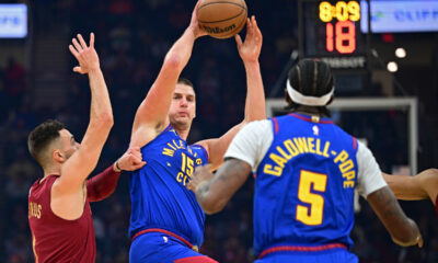Denver Nuggets center Nikola Jokic, center, attempts to pass to Kentavious Caldwell-Pope while being defended by Cleveland Cavaliers guard Max Strus in the first half of an NBA basketball game, Sunday, Nov. 19, 2023, in Cleveland. (AP Photo/David Dermer)