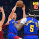 Denver Nuggets center Nikola Jokic, center, attempts to pass to Kentavious Caldwell-Pope while being defended by Cleveland Cavaliers guard Max Strus in the first half of an NBA basketball game, Sunday, Nov. 19, 2023, in Cleveland. (AP Photo/David Dermer)
