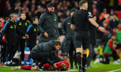 Liverpool's Kostas Tsimikas, bottom, grimaces in pain after a tackle by Arsenal's Bukayo Saka during the English Premier League soccer match between Liverpool and Arsenal at Anfield stadium in Liverpool, England, Saturday, Dec. 23, 2023. (AP Photo/Jon Super)