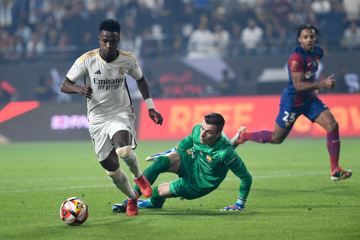 Real Madrid's Vinicius Junior, left, passes through Barcelona's goalkeeper Inaki Pena during the Spanish Super Cup final soccer match between Real Madrid and Barcelona at Al-Awwal Park Stadium in Riyadh, Saudi Arabia, Sunday, Jan. 14, 2024. (AP Photo)