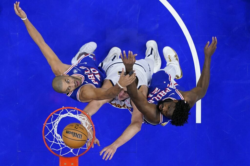 Denver Nuggets' Nikola Jokic, center, goes up for a shot against Philadelphia 76ers' Nicolas Batum, left, and Joel Embiid during the second half of an NBA basketball game, Tuesday, Jan. 16, 2024, in Philadelphia. (AP Photo/Matt Slocum)