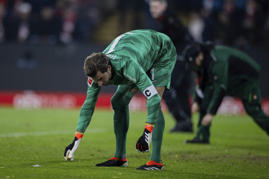 Frankfurt goalkeeper Kevin Trapp collects chocolate coins thrown onto the pitch by fans in protest against a DFL investor during the Bundesliga soccer match between FC Koln and Eintracht Frankfurt at the RheinEnergieStadion in Cologne, Germany, Saturday Feb. 3, 2024. (Rolf Vennenbernd/dpa via AP)