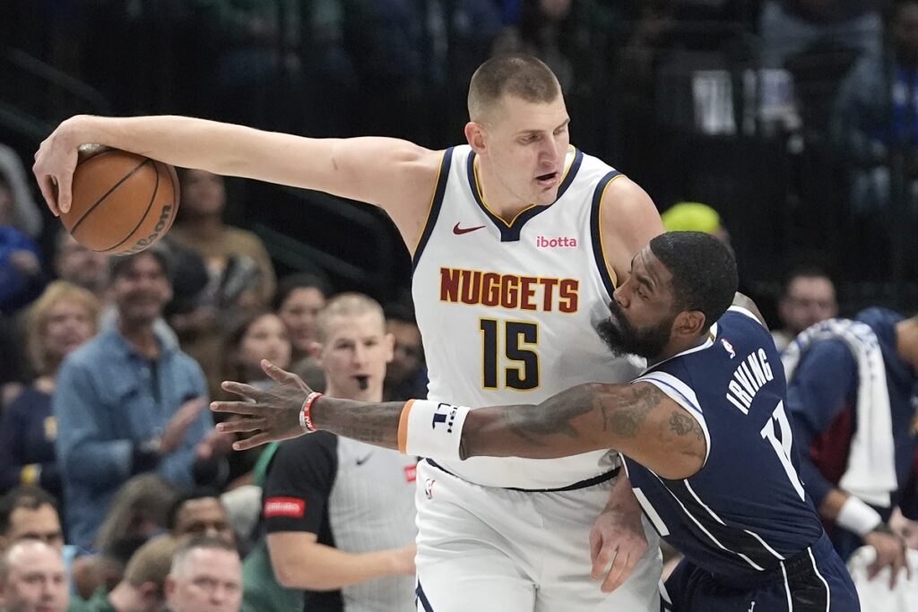 Denver Nuggets center Nikola Jokic (15) keeps the ball out of reach against Dallas Mavericks guard Kyrie Irving (11) during the first half of an NBA basketball game in Dallas, Sunday, March 17, 2024. (AP Photo/LM Otero)