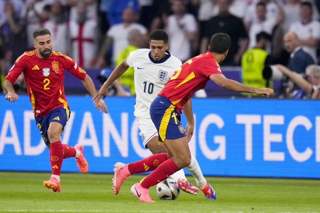 England's Jude Bellingham tries to drive the ball past Spain's Dani Carvajal, left, and Rodri during the final match between Spain and England at the Euro 2024 soccer tournament in Berlin, Germany, Sunday, July 14, 2024. (AP Photo/Manu Fernandez)