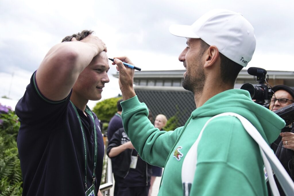 Serbia's Novak Djokovic signs a fan's forehead as he makes his way to a training session, a day ahead of his Men's singles final match against Spain's Carlos Alcaraz at the Wimbledon tennis championships, in London, Saturday, July 13, 2024. (Aaron Chown/PA via AP)