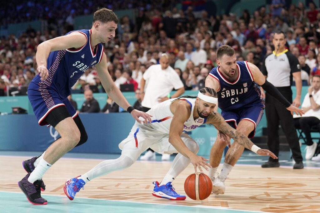 Jose Alvarado, of Puerto Rico, dives for a loose ball between Nikola Jovic and Marko Guduric, of Serbia, in a men's basketball game at the 2024 Summer Olympics, Wednesday, July 31, 2024, in Villeneuve-d'Ascq, France. (AP Photo/Mark J. Terrill)