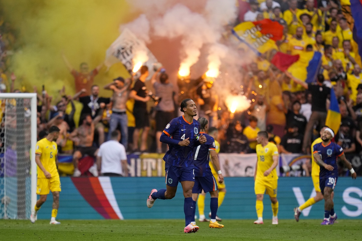 Virgil van Dijk of the Netherlands, center, runs while Romania supporters light flares on the stands during a round of sixteen match between Romania and the Netherlands at the Euro 2024 soccer tournament in Munich, Germany, Tuesday, July 2, 2024. (AP Photo/Manu Fernandez)