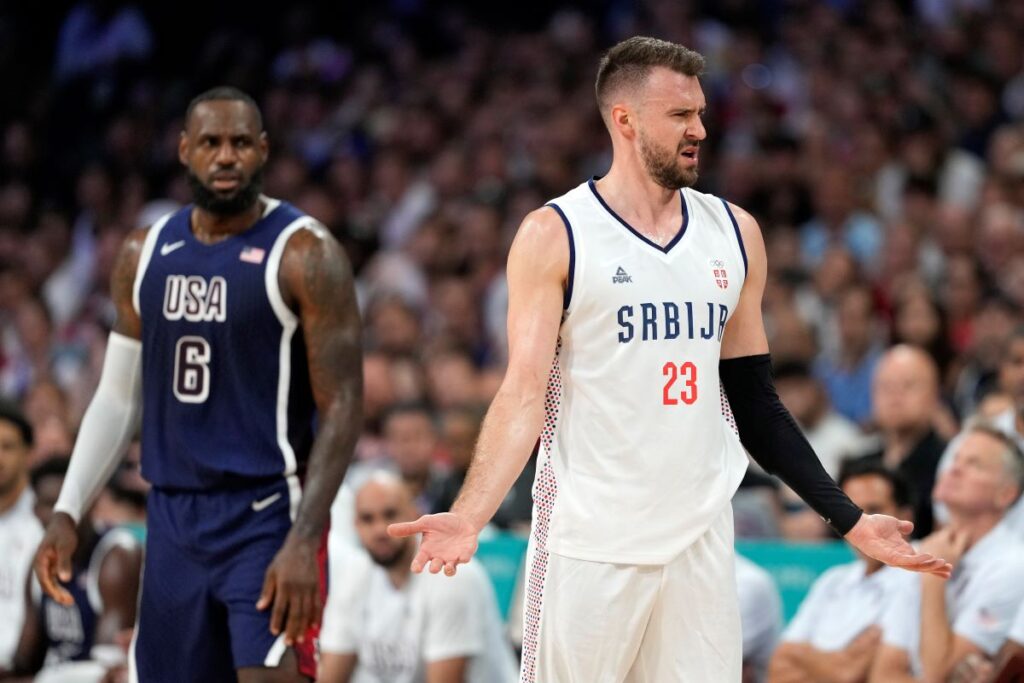 Marko Guduric, right, of Serbia, complains about being called for a foul as LeBron James, of the United States, looks on in a men's basketball game at the 2024 Summer Olympics, Sunday, July 28, 2024, in Villeneuve-d'Ascq, France. (AP Photo/Michael Conroy)