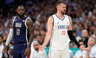 Marko Guduric, right, of Serbia, complains about being called for a foul as LeBron James, of the United States, looks on in a men's basketball game at the 2024 Summer Olympics, Sunday, July 28, 2024, in Villeneuve-d'Ascq, France. (AP Photo/Michael Conroy)