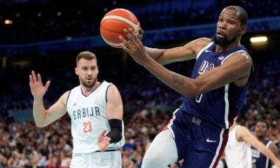 Kevin Durant, right, of the United States, passes the ball as he heads out of bounds while under pressure from Marko Guduric, of Serbia, in a men's basketball game at the 2024 Summer Olympics, Sunday, July 28, 2024, in Villeneuve-d'Ascq, France. (AP Photo/Michael Conroy)