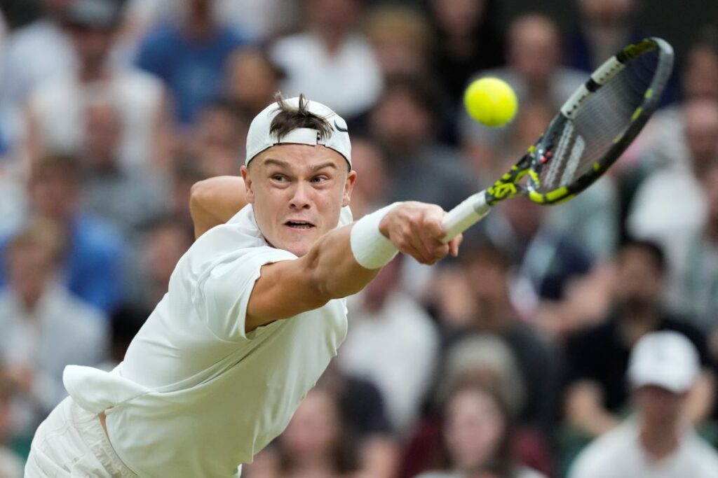 Hulger Rune of Denmark plays a backhand return to Novak Djokovic of Serbia during their fourth round match at the Wimbledon tennis championships in London, Monday, July 8, 2024. (AP Photo/Kirsty Wigglesworth)