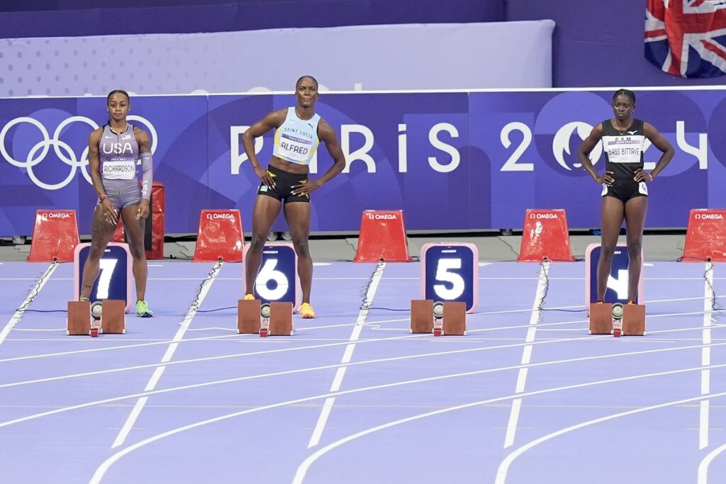 Sha'carri Richardson, of the United States, left, and Julien Alfred, of Saint Lucia, stand next to an empty lane 5 after Shelly-Ann Fraser-Pryce, of Jamaica, withdrew from a women's 100 meters semifinal at the 2024 Summer Olympics, Saturday, Aug. 3, 2024, in Saint-Denis, France.(AP Photo/Martin Meissner)