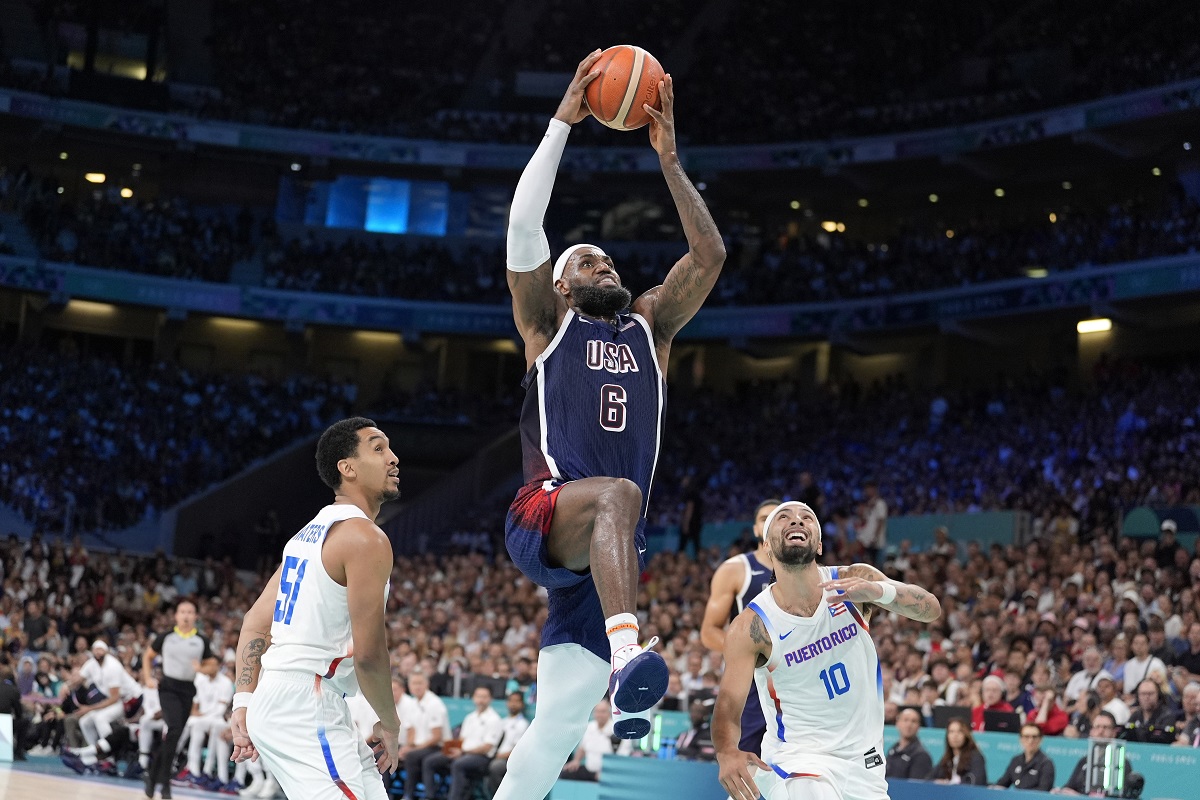 United States' LeBron James, center, goes up for a dunk as Puerto Rico's Tremont Waters, left, and Puerto Rico's Jose Alvarado defend during a men's basketball game at the 2024 Summer Olympics, Saturday, Aug. 3, 2024, in Villeneuve-d'Ascq, France. (AP Photo/Michael Conroy)