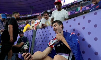 Hamish Kerr, of New Zealand, uses a cellphone while sitting by the stands after winning the gold medal in the men's high jump final at the 2024 Summer Olympics, Saturday, Aug. 10, 2024, in Saint-Denis, France. (AP Photo/Ashley Landis)