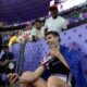 Hamish Kerr, of New Zealand, uses a cellphone while sitting by the stands after winning the gold medal in the men's high jump final at the 2024 Summer Olympics, Saturday, Aug. 10, 2024, in Saint-Denis, France. (AP Photo/Ashley Landis)