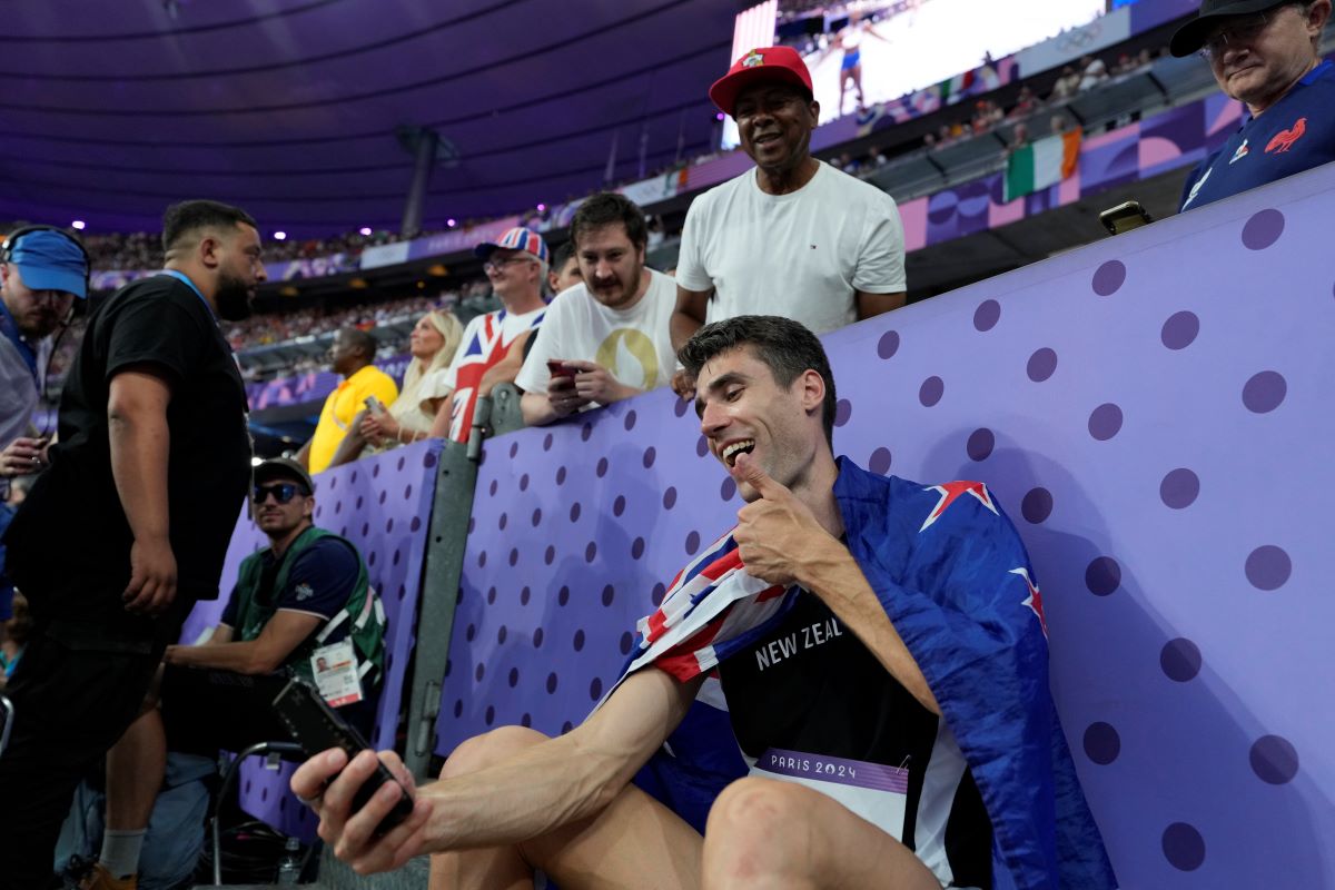 Hamish Kerr, of New Zealand, uses a cellphone while sitting by the stands after winning the gold medal in the men's high jump final at the 2024 Summer Olympics, Saturday, Aug. 10, 2024, in Saint-Denis, France. (AP Photo/Ashley Landis)