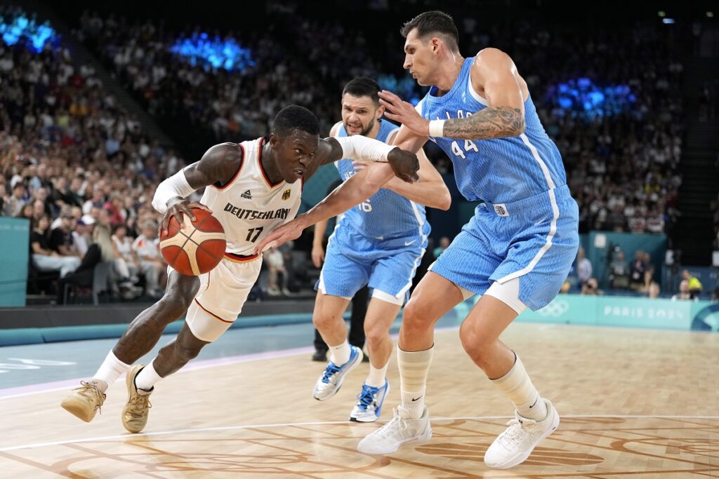 Germany's Dennis Schroder, left, tries to drive by Greece's Kostas Papanikolaou, center, and Greece's Dinos Mitoglou during a men's basketball game at the 2024 Summer Olympics, Tuesday, Aug. 6, 2024, in Villeneuve-d'Ascq, France. (AP Photo/Michael Conroy)