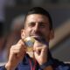 Serbia's Novak Djokovic shows his gold medal after defeating Spain's Carlos Alcaraz in the men's singles tennis final at the Roland Garros stadium during the 2024 Summer Olympics, Sunday, Aug. 4, 2024, in Paris, France. Djokovic has won his first Olympic gold medal by beating Alcaraz 7-6 (3), 7-6 (2) in the 2024 Games men's tennis singles final. (AP Photo/Manu Fernandez)