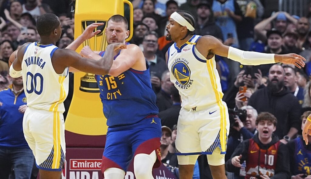 Denver Nuggets center Nikola Jokic, center, is fouled while going up for a basket between Golden State Warriors forward Jonathan Kuminga, left, and guard Moses Moody in the second half of an Emirates NBA Cup basketball game Tuesday, Dec. 3, 2024, in Denver. (AP Photo/David Zalubowski)