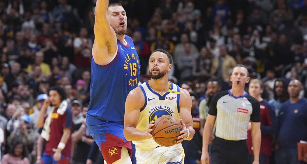 Golden State Warriors guard Stephen Curry, right, drives past Denver Nuggets center Nikola Jokic to put up a last-second, 3-point shot in the second half of an Emirates NBA Cup basketball game Tuesday, Dec. 3, 2024, in Denver. (AP Photo/David Zalubowski)