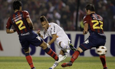 FILE - Brazil's Santos' Neymar, center, kicks the ball to score as Paraguay's Cerro Porteno's players Cesar Benitez, left, and Mariano Uglessich fail to block during a Copa Libertadores soccer game in Asuncion, Paraguay, Wednesday, June 1, 2011. (AP Photo/Cesar Olmedo, File)