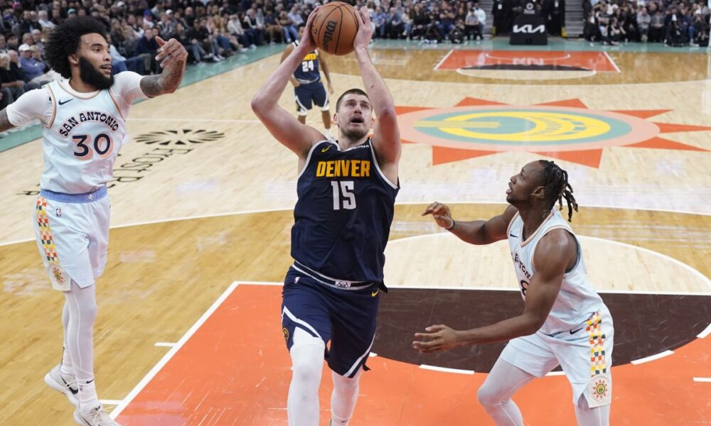 Denver Nuggets center Nikola Jokic (15) drives to the basket past San Antonio Spurs forward Julian Champagnie (30) and center Charles Bassey, right, during the first half of an NBA basketball game in San Antonio, Saturday, Jan. 4, 2025. (AP Photo/Eric Gay)