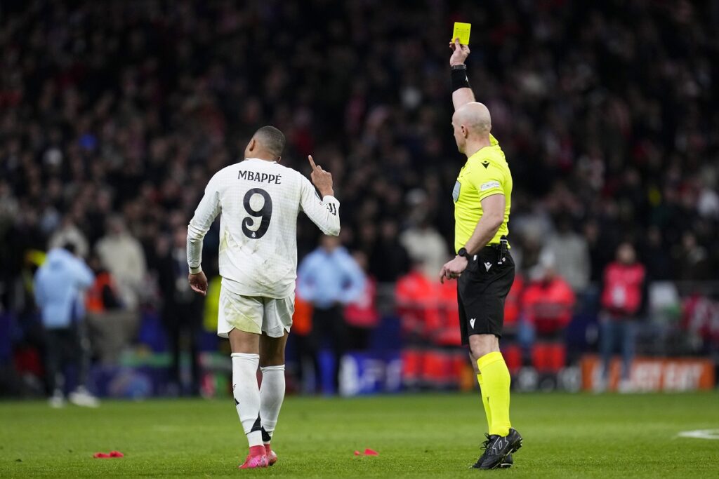 Referee Szymon Marciniak shows a yellow card to Real Madrid's Kylian Mbappe during the Champions League round of 16, second leg, soccer match between Atletico Madrid and Real Madrid at the Metropolitano stadium in Madrid, Spain, Wednesday, March 12, 2025. (AP Photo/Manu Fernandez)