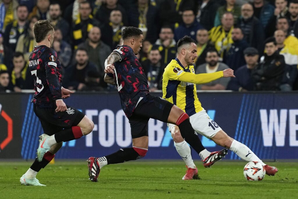 Fenerbahce's Filip Kostic, right, attempts a shot at goal in front of Rangers' James Tavernier, center, and Rangers' Ridvan Yilmaz during the Europa League round of 16 first leg soccer match between Fenerbahce and Rangers at Sukru Saracoglu stadium in Istanbul, Turkey, Thursday, March 6, 2025. (AP Photo/Khalil Hamra)