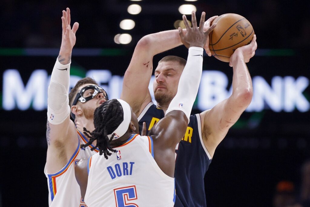 Denver Nuggets center Nikola Jokic, back right, looks to pass the ball away from Oklahoma City Thunder guard Luguentz Dort, center, and center Isaiah Hartenstein, back left, during the first half of an NBA basketball game Monday, March 10, 2025, in Oklahoma City. (AP Photo/Nate Billings)